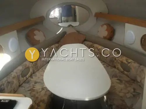 Four Winns 238 Vista: forward cabin with V-shaped floral settee around an oval white table and oval mirror
