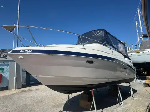 Glastron GT 249: port bow view ashore on stands, showing hull stripe, name and full canopy