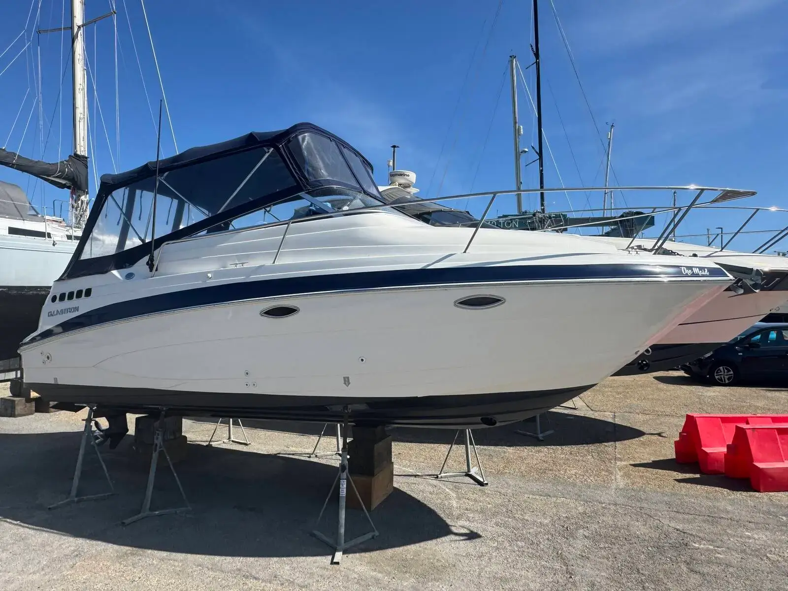 Glastron GT 249: white hull with navy stripe and dark canopy, ashore on stands in a boatyard