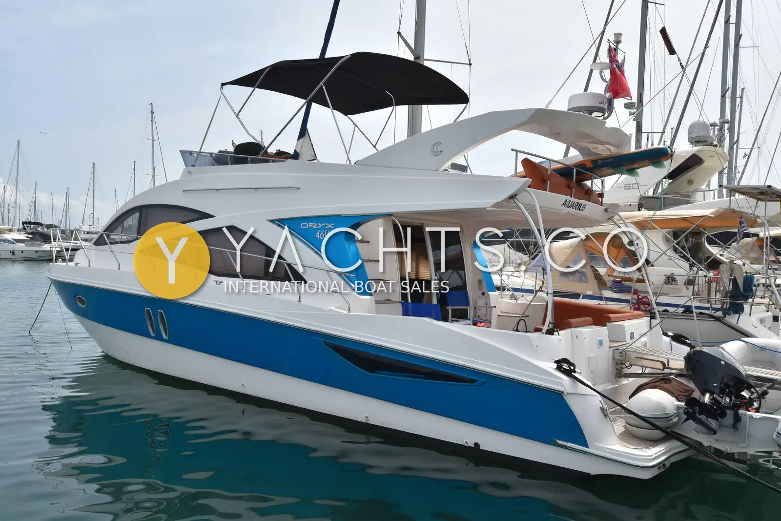 Gulf Craft Oryx 46 Fly: starboard side of the white and blue hull with a bimini over the flybridge, moored in a marina