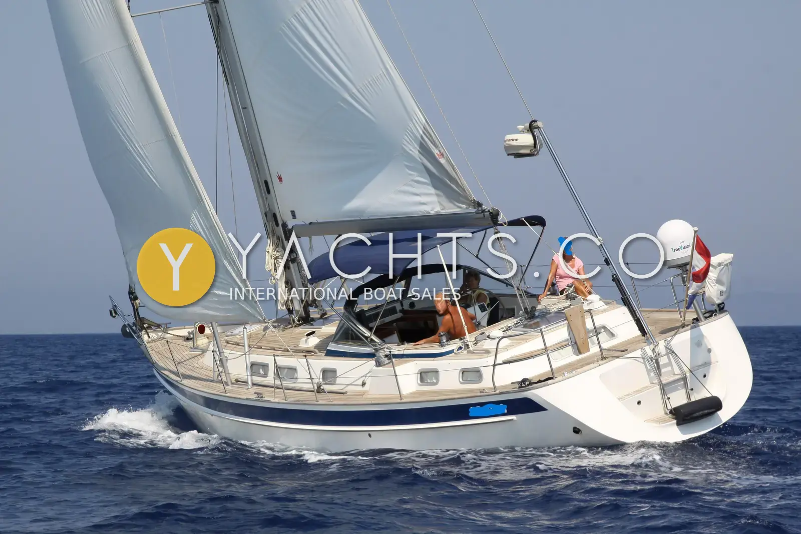 Hallberg-Rassy 43: under full sail heeling at sea, blue bimini, satellite dome and radar on stern pole