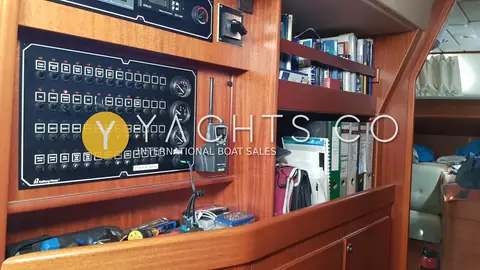 Hallberg-Rassy 43: mahogany switch panel with breakers and gauges beside bookshelves and handheld VHF