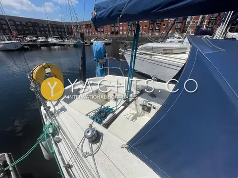 Hanse 301: cockpit looking aft with tiller, horseshoe lifebuoy, mainsheet traveller and marina buildings beyond