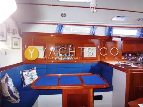 Hanse 341 Yacht For Sale: saloon L-shaped settee with blue place mats on table, mahogany lockers and book shelf
