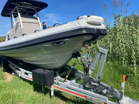 Highfield 900 Sport: stern quarter on twin axle trailer ashore, grey hull and tubes beside tall grass