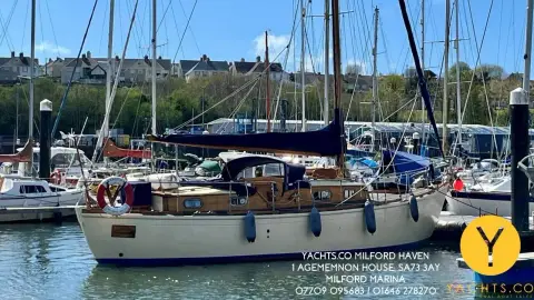 Hillyard 12 Ton: classic yacht afloat in the marina, showing centre cockpit spray hood and varnished coachroof