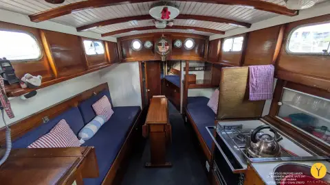 Hillyard 12 Ton: saloon with blue upholstered settees, varnished mahogany joinery, central table and galley to starboard