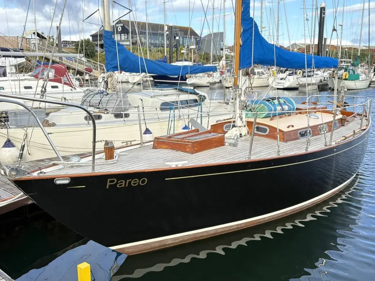 Holman Twister 28: dark blue hull with 'Pareo' on the bow and varnished coachroof, afloat in a marina
