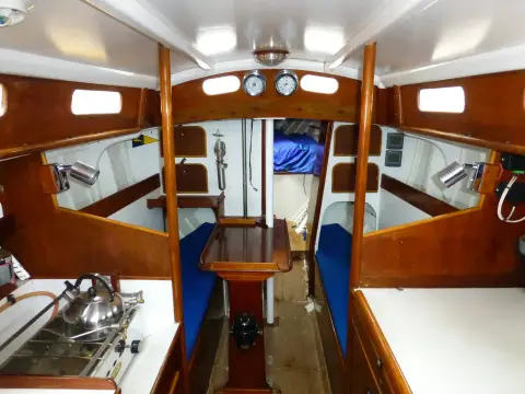 Holman Twister 28: saloon looking forward with blue bench berths, varnished joinery and central drop-leaf table