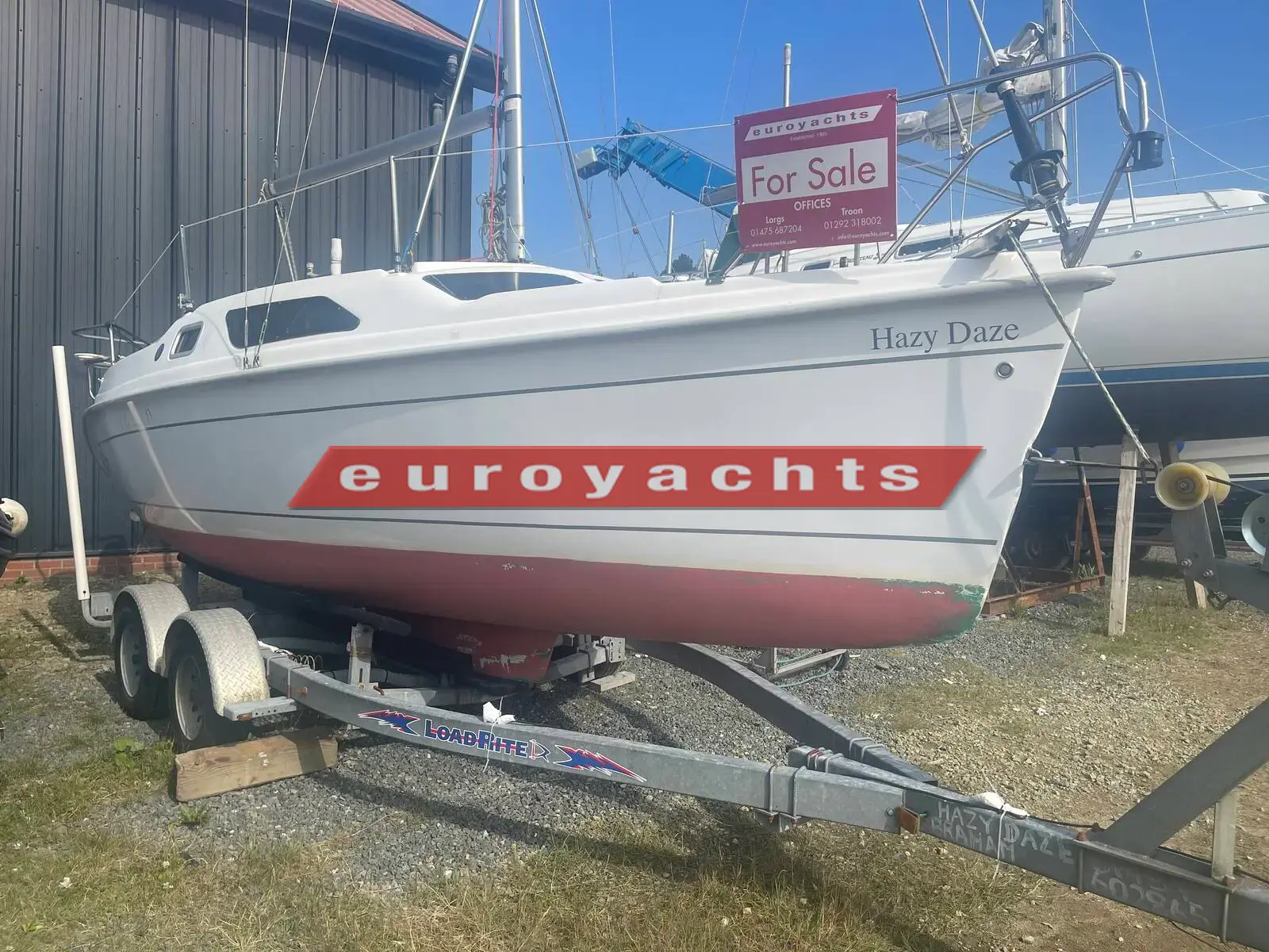 Hunter Legend 25 Trailer Sailer: white hull with red antifouling on a tandem-axle trailer beside a shed, for-sale sign aboard