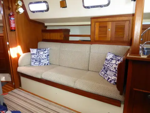 Island Packet 320: port saloon settee in cream upholstery with patterned cushions beneath portlights and lockers