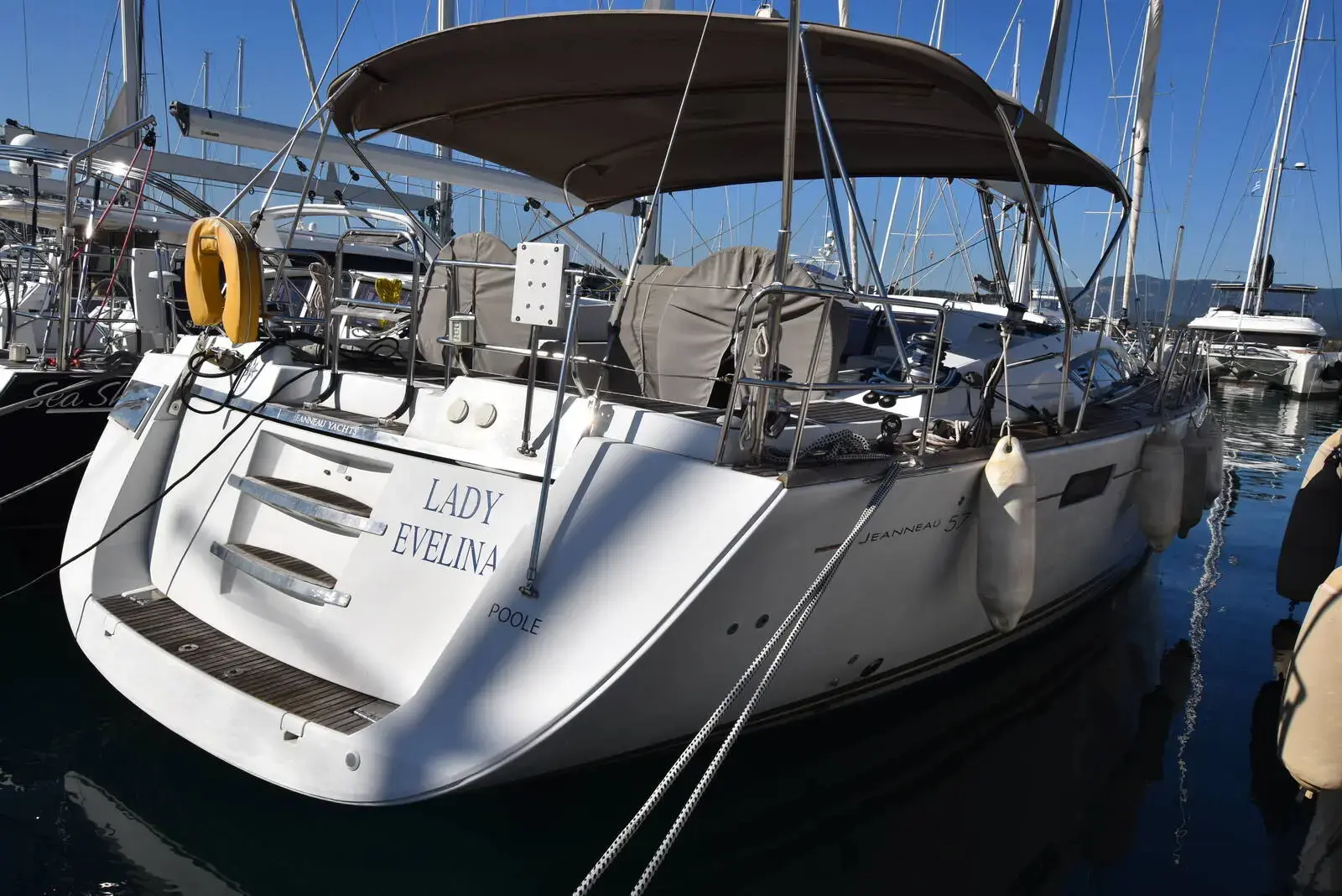 Jeanneau 57: stern quarter view of white hull with bimini, bathing platform steps and lifebuoy, moored in marina