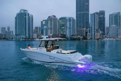 Jeanneau Cap Camarat 10.5 CC: underway at dusk past city towers, purple underwater lights glowing at the stern