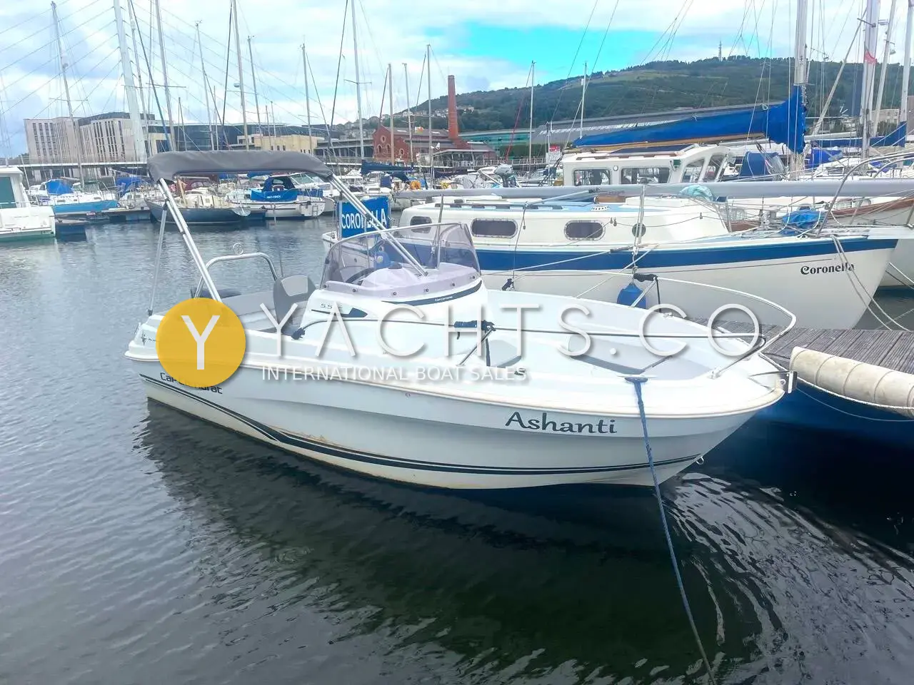 Jeanneau Cap Camarat 5.5 CC: white hull moored in marina with hills behind, towing arch and console visible