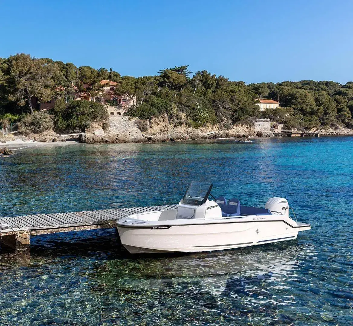 Jeanneau Cap Camarat 6.0 CC: white-hulled centre-console boat moored at a wooden jetty in clear turquoise water by a wooded shore