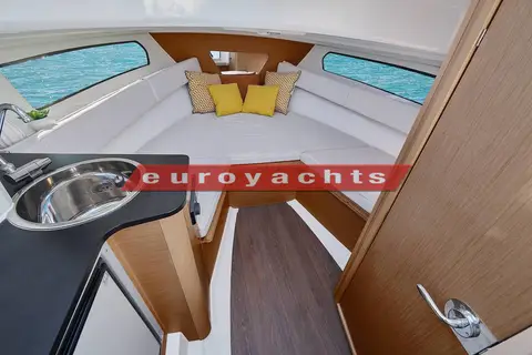 Jeanneau Cap Camarat 7.5 WA: cabin with a white U-shaped settee, wood trim, large hull windows and a galley sink