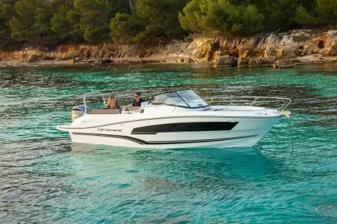 Jeanneau Cap Camarat 7.5 WA: boat at anchor in clear turquoise water off a rocky, pine-covered shore