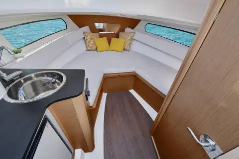 Jeanneau Cap Camarat 7.5 WA: cabin interior with U-shaped white upholstered seating, hull windows and wood trim, sink in foreground