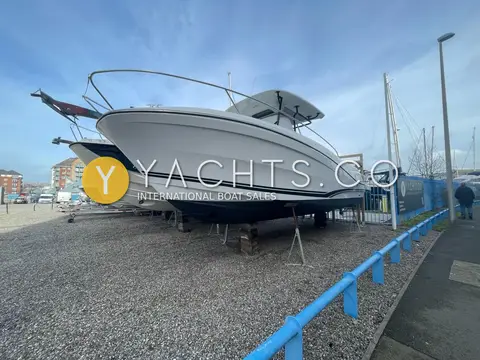 Jeanneau Cap Camarat 9.0 CC: hull ashore on chocks and stands beside another sports boat, black T-top and bow rail visible