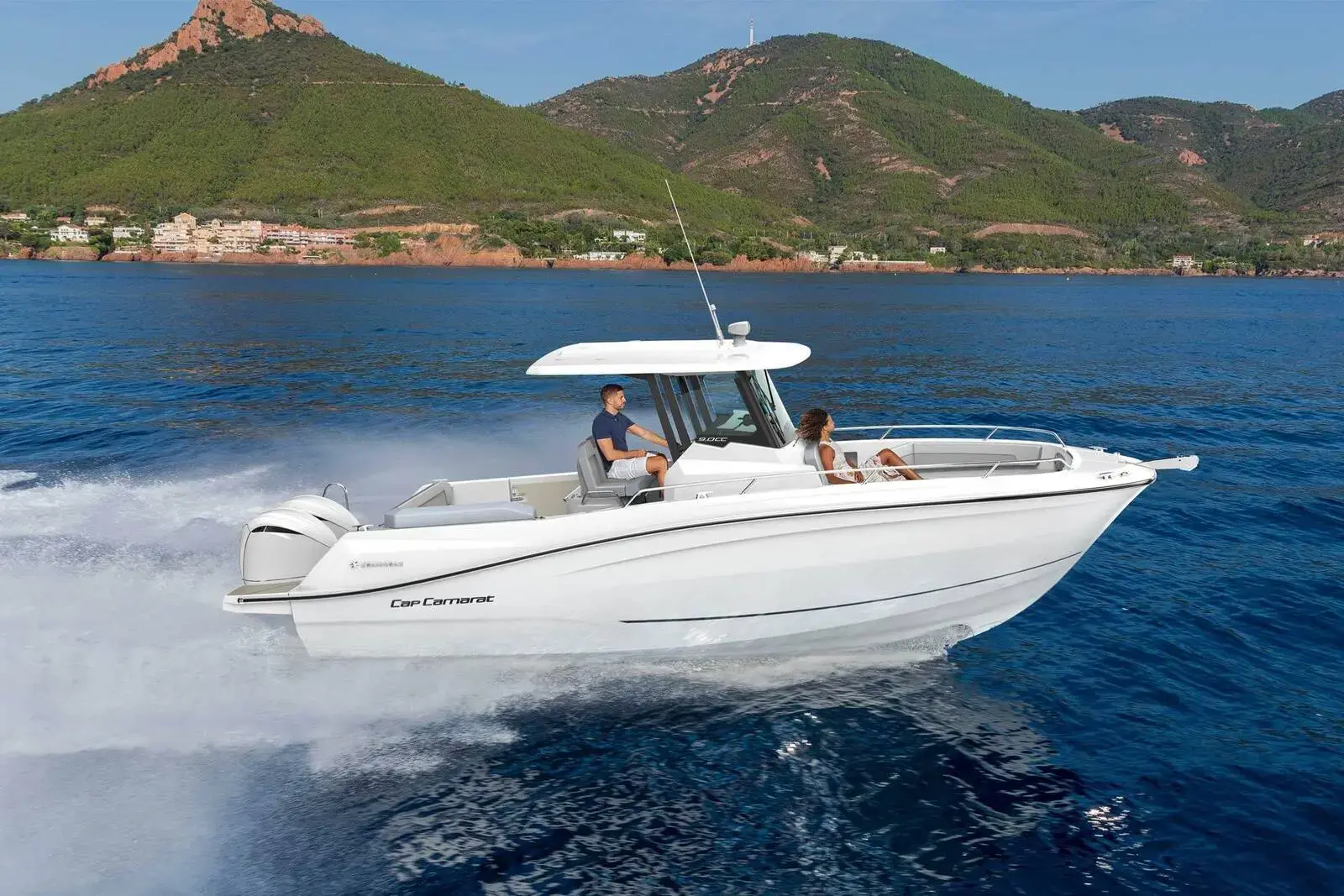 Jeanneau Cap Camarat 9.0 CC Series 2: white centre console boat with hard top under way at speed near a green hilly coastline