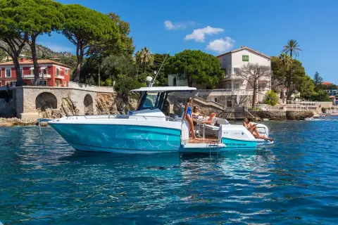Jeanneau Cap Camarat 9.0 CC: teal hull anchored near a waterfront village with guests relaxing in the aft cockpit
