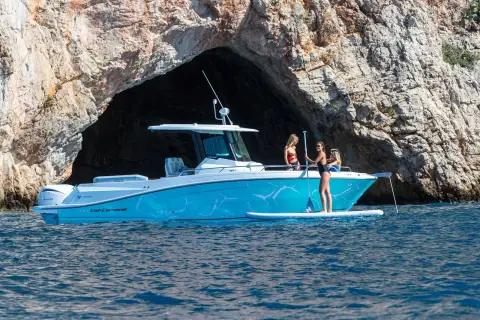 Jeanneau Cap Camarat 9.0 CC Serie 2: turquoise hull at anchor beside a sea cave with a paddleboarder alongside
