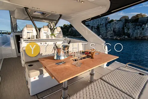 Jeanneau DB 37: cockpit with wooden dining table, bench seating and hardtop overhead beside cliffs