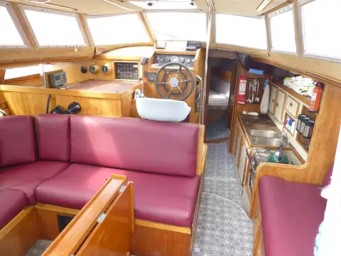 Jeanneau Espace 1000: wheelhouse with burgundy L-shaped seating, inside wheel helm and galley to starboard