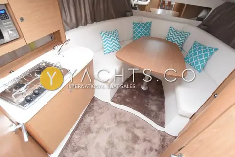 Jeanneau Leader 8: saloon dinette with wooden table, turquoise cushions and galley hob to the left