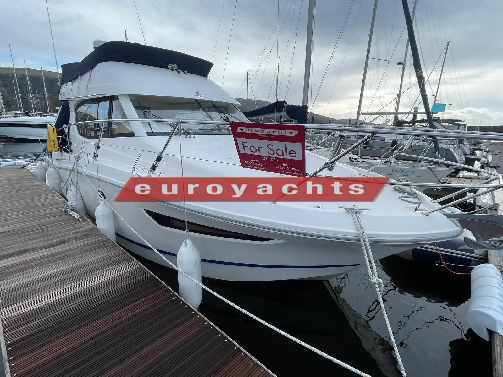 Jeanneau Merry Fisher 10: starboard bow view of the white flybridge motor boat moored on a pontoon with a for sale sign