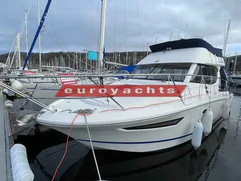 Jeanneau Merry Fisher 10: port bow view of the hull and flybridge canopy in a marina with hills behind