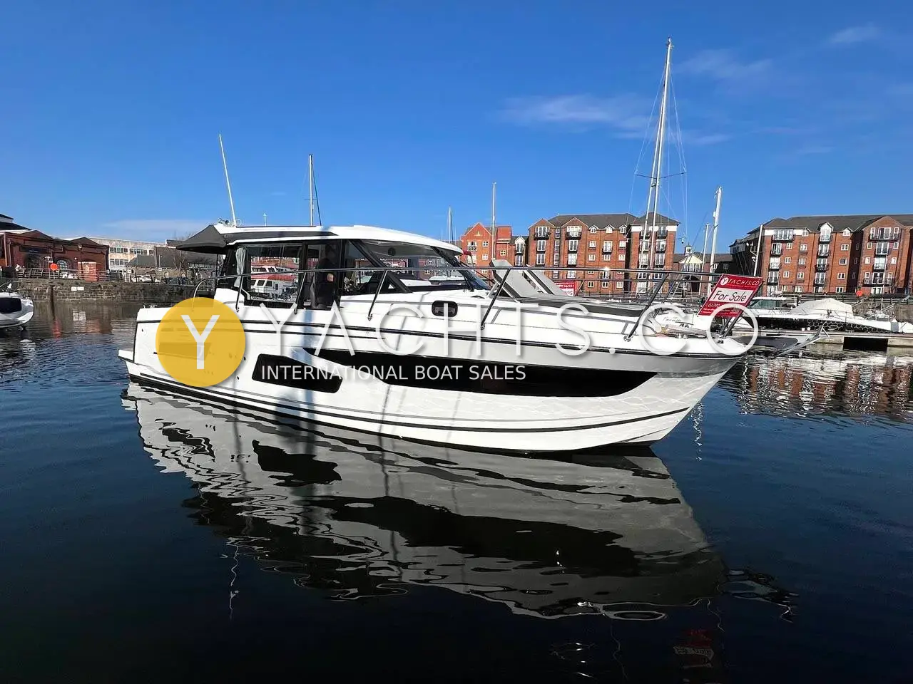 Jeanneau Merry Fisher 1095: starboard side of the white hull with dark window band, moored in a marina beside flats