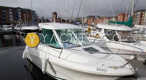Jeanneau Merry Fisher 585: starboard bow view of the white wheelhouse boat moored in a marina beside red-brick buildings