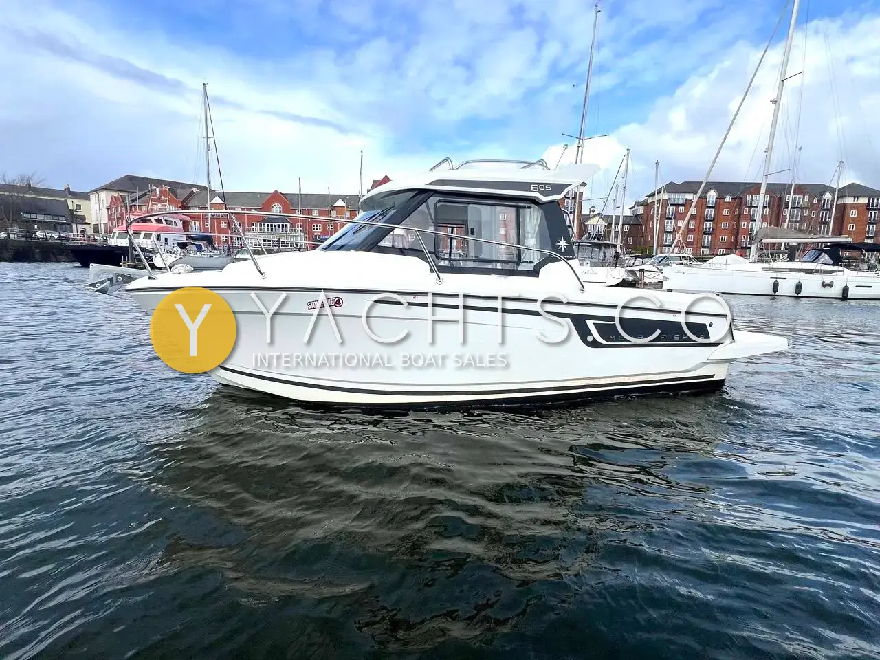 Jeanneau Merry Fisher 605 S2: white hull with dark side window stripe, afloat in a marina with brick buildings behind