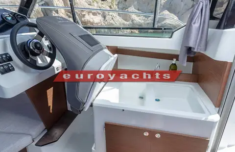 Jeanneau Merry Fisher 605 Serie 2: galley unit with sink and wood-effect cabinetry beside the helm seat inside the wheelhouse