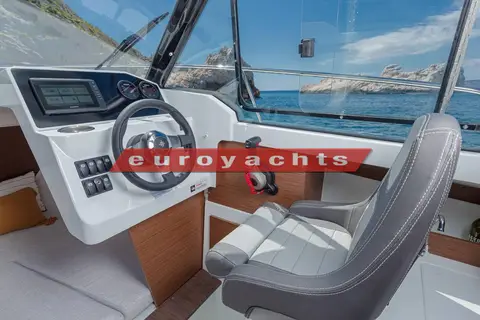 Jeanneau Merry Fisher 605 Serie 2: helm station with wheel, chartplotter display and grey helm seat facing large wheelhouse windows
