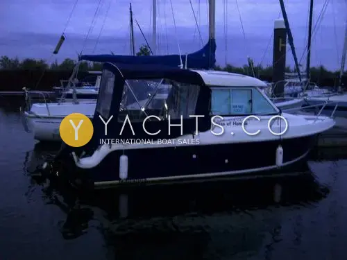 Jeanneau Merry Fisher 625 Legend: navy-hulled wheelhouse boat at dusk in a marina, rear canopy closed, outboard on the transom