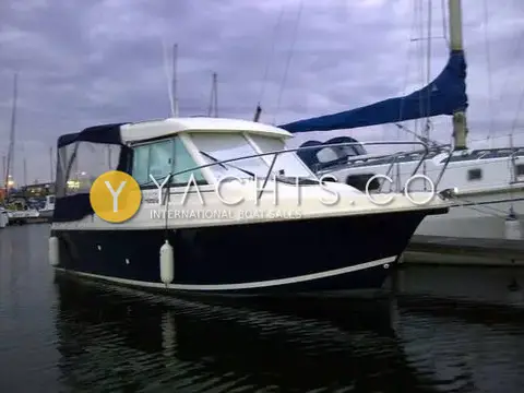 Jeanneau Merry Fisher 625 Legend: bow quarter view of navy hull with white topsides, fenders out, moored alongside a pontoon