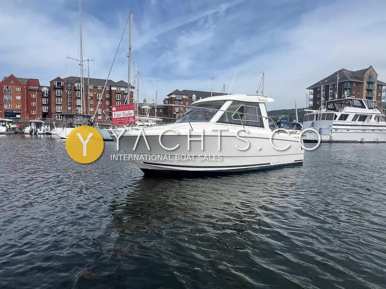 Jeanneau Merry Fisher 645: white wheelhouse motor boat afloat in a marina basin, with brick apartment buildings behind