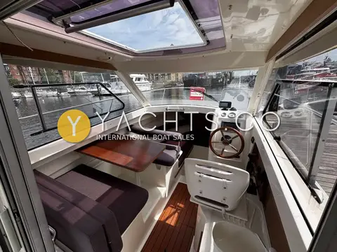 Jeanneau Merry Fisher 645: wheelhouse interior with open sunroof, dinette seating, wooden table and helm to starboard