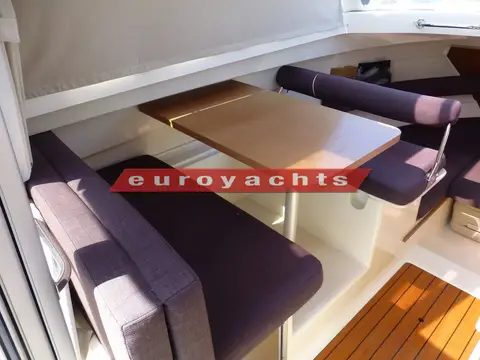Jeanneau Merry Fisher 645: dining area with wooden table between purple fore and aft bench seats