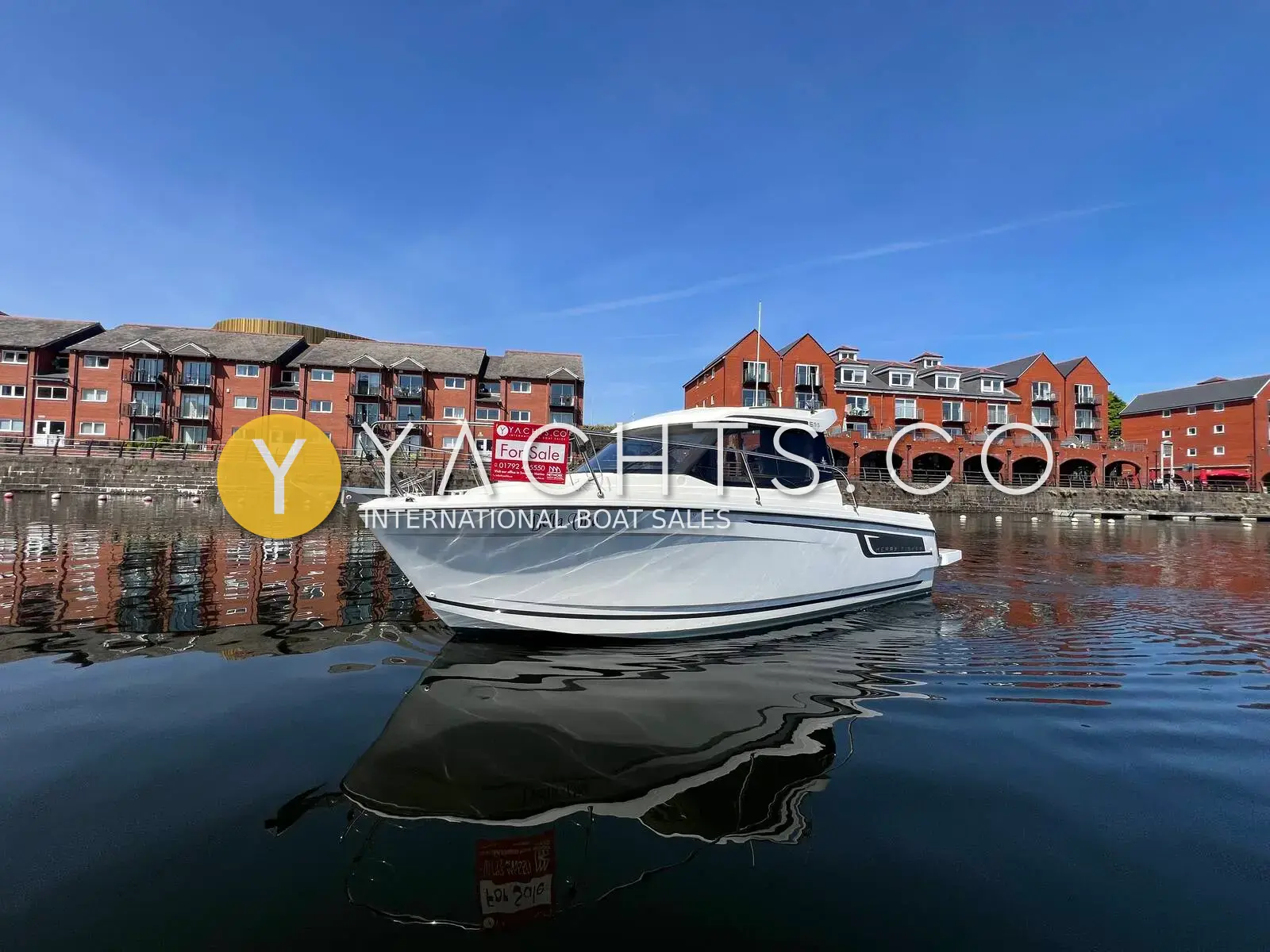 Jeanneau Merry Fisher 695: white hull afloat in a marina basin beside red-brick waterfront flats under blue sky
