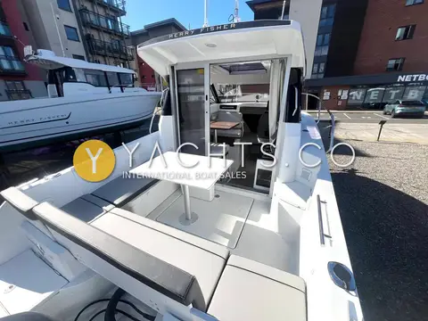 Jeanneau Merry Fisher 695: aft cockpit with grey cushioned seating and white table, wheelhouse door open