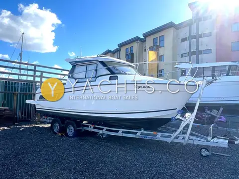 Jeanneau Merry Fisher 695: bow quarter view of the hull on her trailer beside waterfront apartments