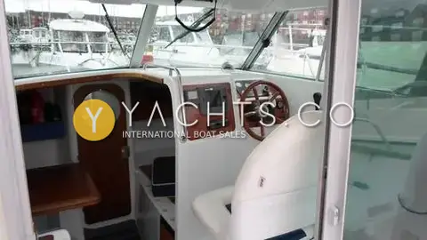 Jeanneau Merry Fisher 695: wheelhouse interior with wooden wheel, chart display, white helm seat and heads door forward
