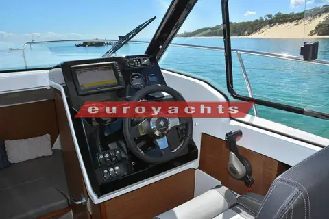 Jeanneau Merry Fisher 695: wheelhouse helm with chartplotter screen, steering wheel and side window open to the shore