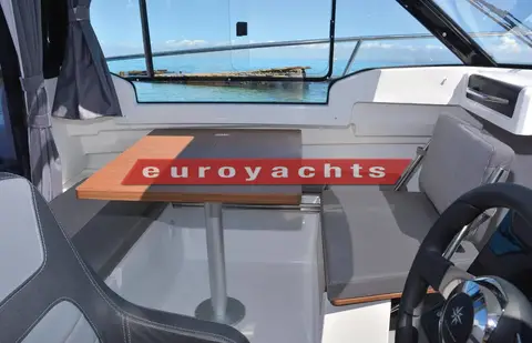Jeanneau Merry Fisher 695: wheelhouse saloon with wood-topped table and grey bench seating facing the windscreen