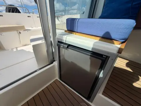 Jeanneau Merry Fisher 725: wheelhouse fridge fitted beneath a blue cushioned seat beside the cockpit door