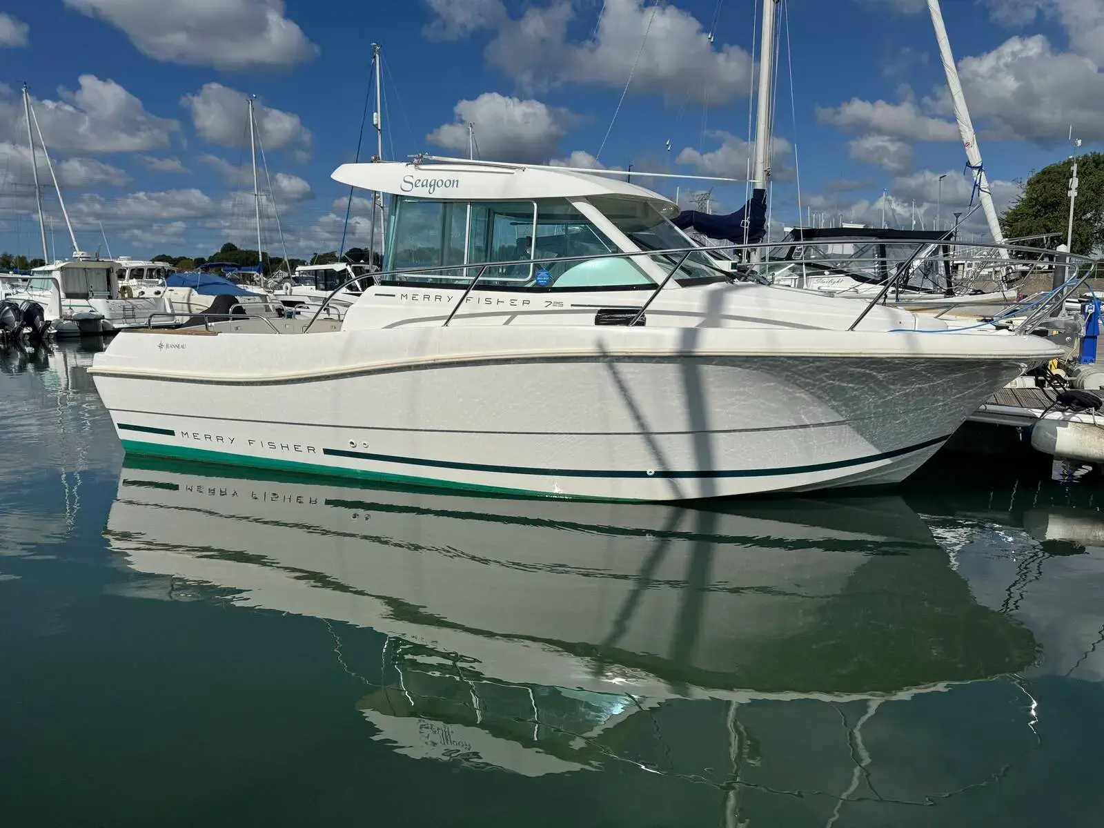 Jeanneau Merry Fisher 725: white hull with green boot stripe and wheelhouse, moored in a marina on calm water