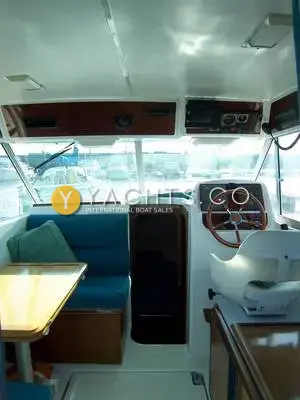 Jeanneau Merry Fisher 750 Reduced: wheelhouse looking forward, with blue dinette seating, wooden table and helm with wooden wheel